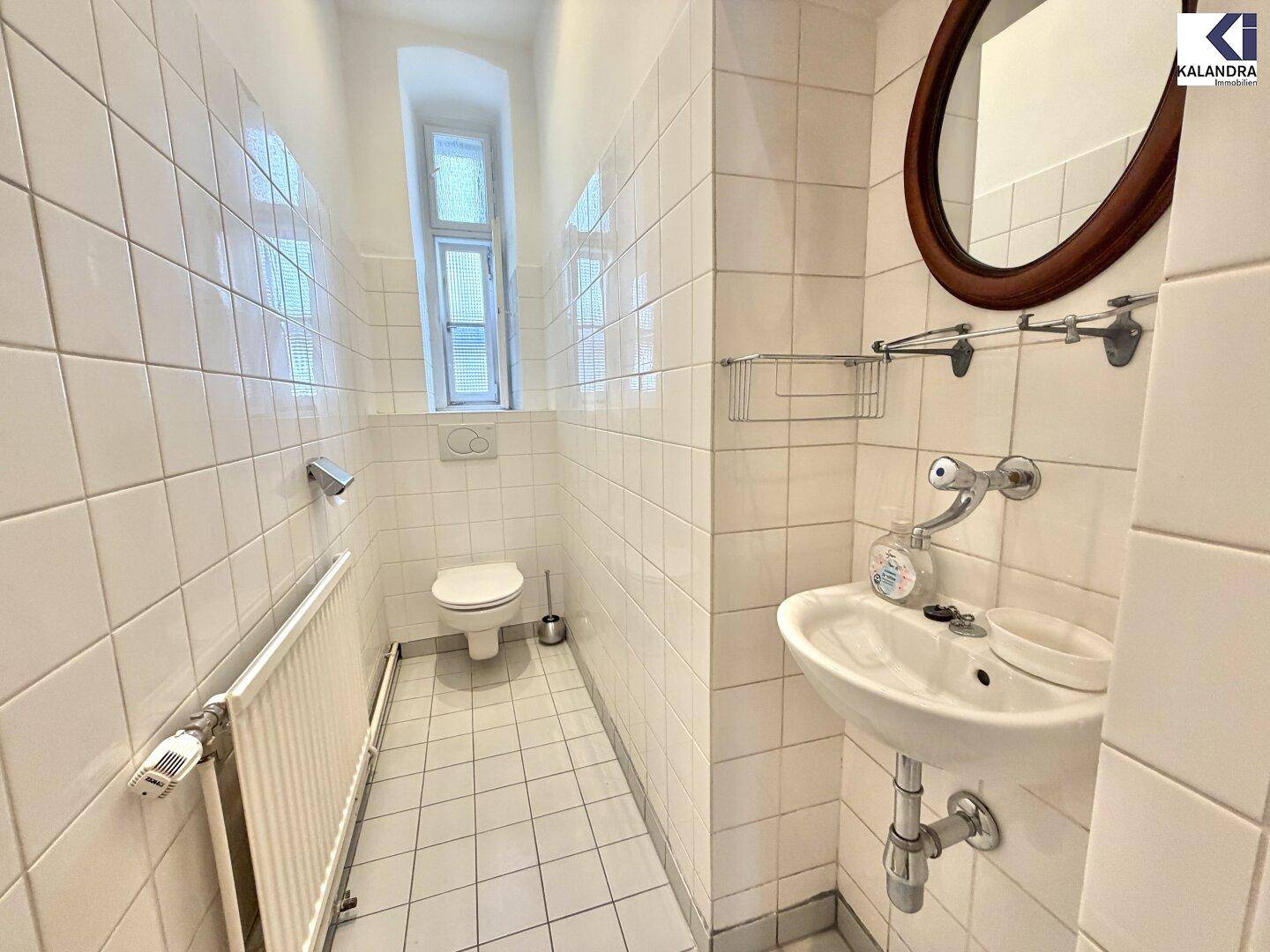 Kleines, gefliestes WC mit Fenster, Wand-WC und Waschbecken, funktional und hell.