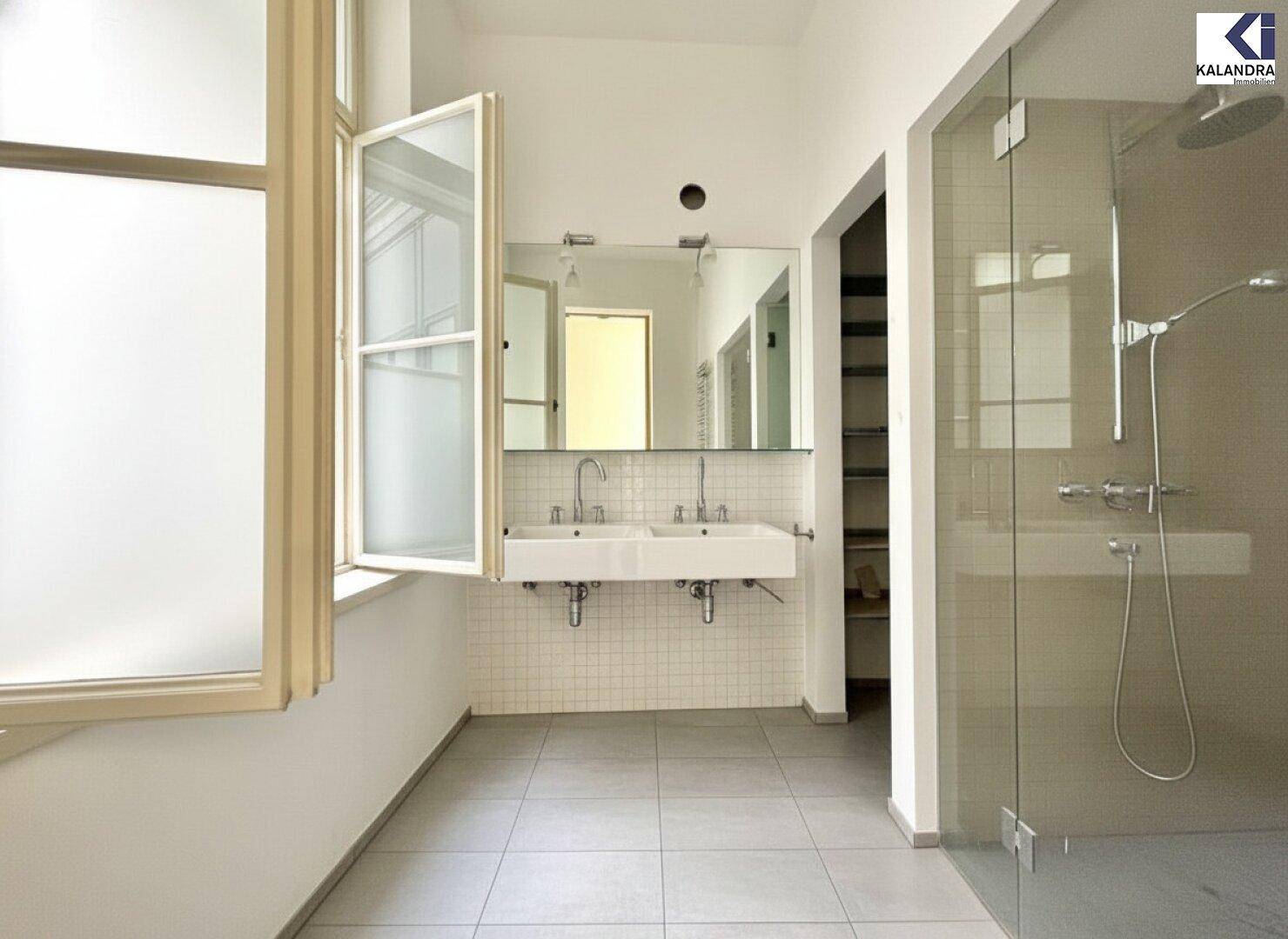 Modernes Badezimmer mit Doppelwaschbecken, großer Duschkabine und einem Fenster für natürliche Belüftung.