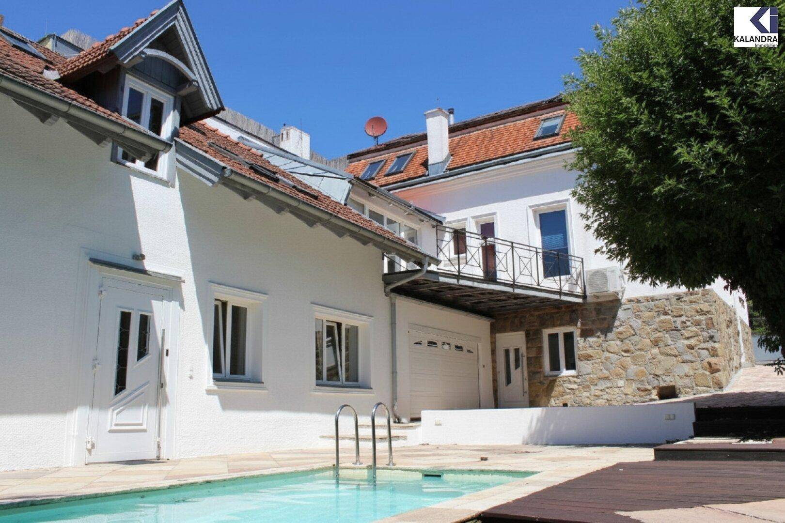 Ansicht des Hauses mit Pool, einer Steinfassade und einem Balkon unter strahlend blauem Himmel.