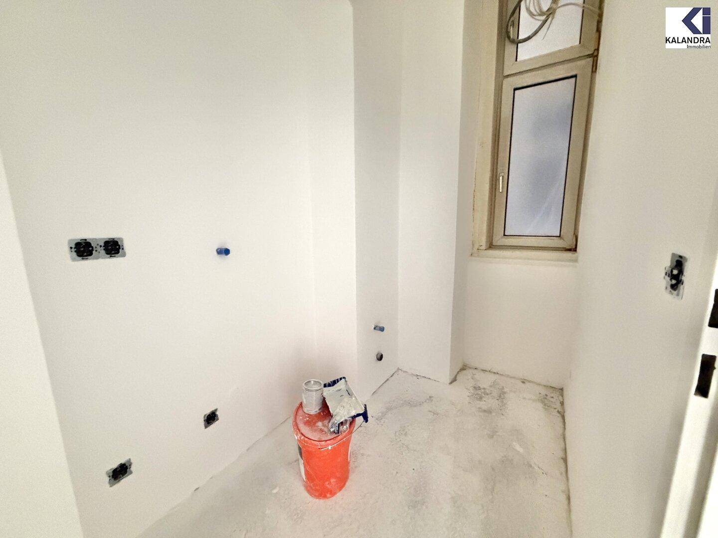 Kleiner Hauswirtschaftsraum im Rohbau mit Fenster, weißen Wänden und sichtbaren Anschlüssen.