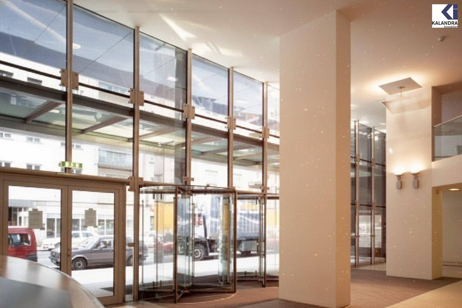 Heller Eingangsbereich mit großen Glasfronten, Drehtüren und Blick auf die Straße, der viel Tageslicht hereinlässt.