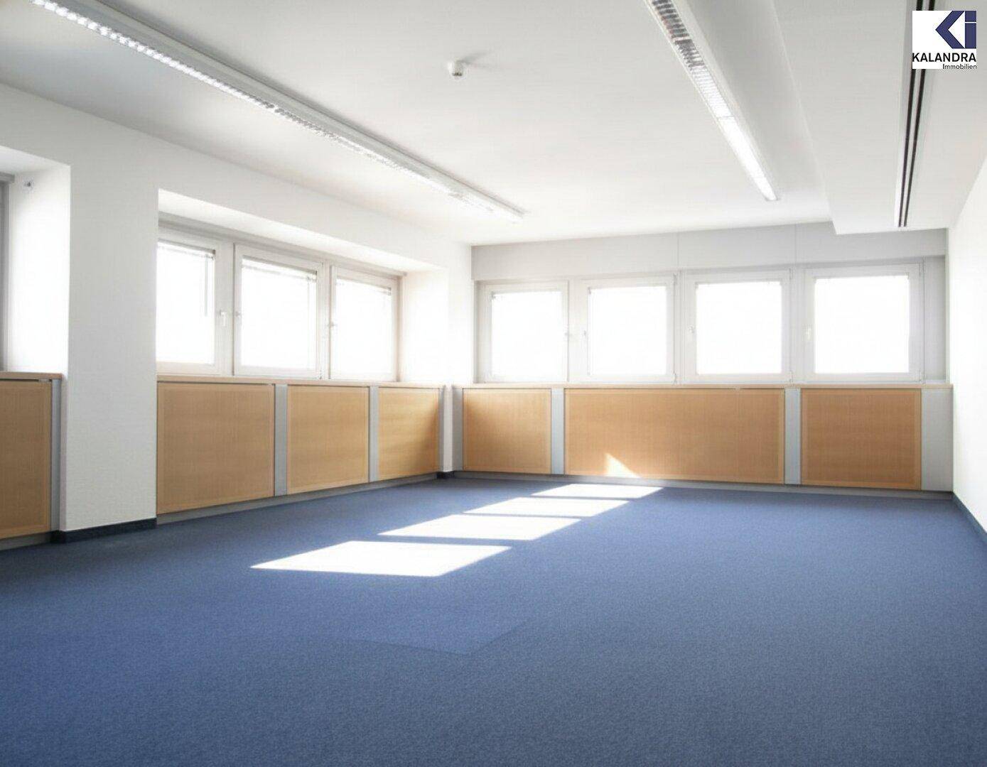 Leeres Büro mit blauem Teppichboden, großen Fenstern und integrierten Holzschränken unter den Fensterbänken.