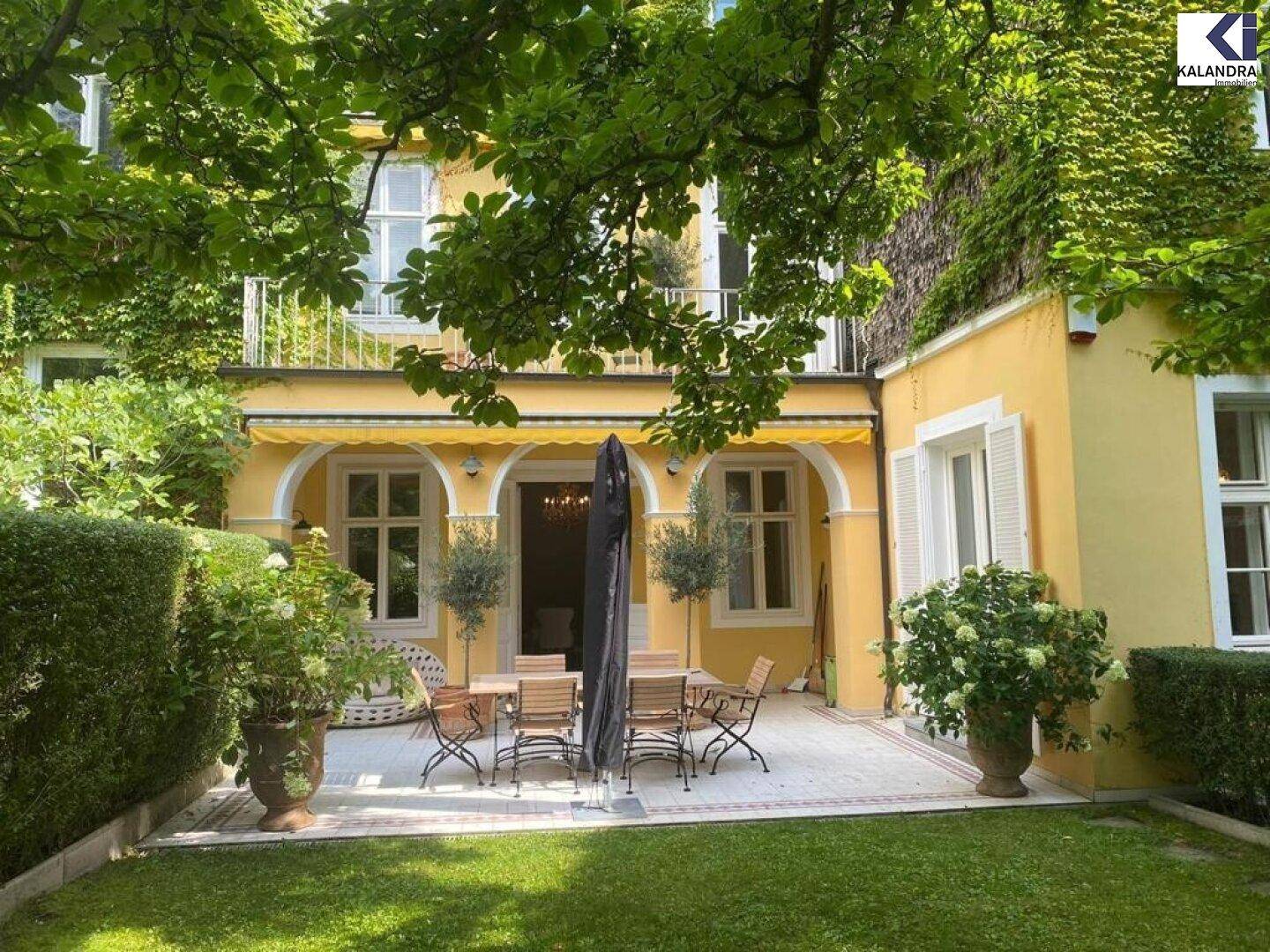 Gepflegter Garten mit großer Terrasse, umgeben von üppigem Grün und schattenspendenden Bäumen.