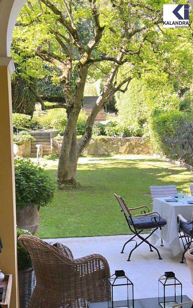 Gemütliche Terrasse mit Korbsesseln und Blick auf den weitläufigen, grünen Garten.
