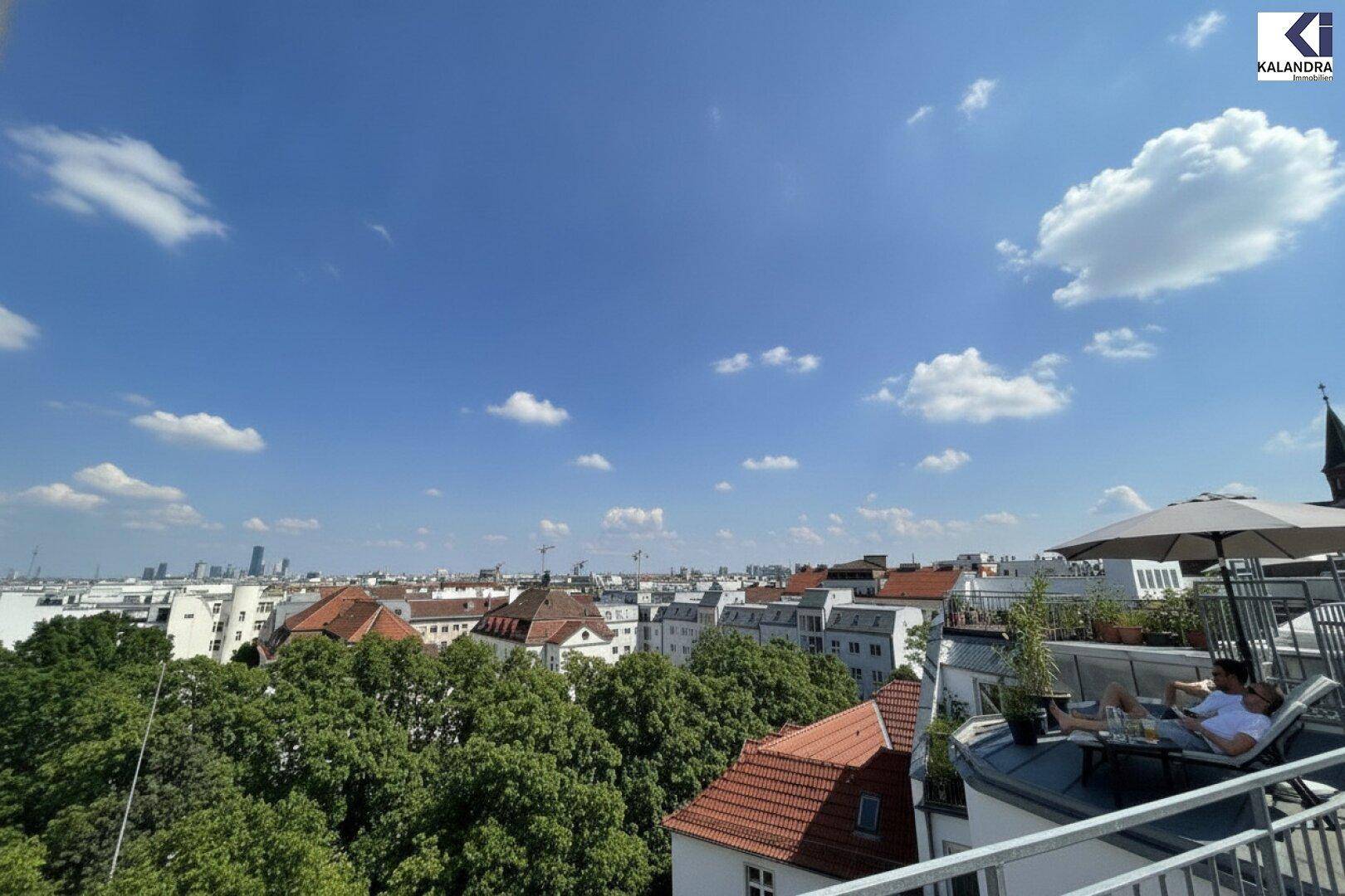 Weitläufiger Blick über die Stadt von einer Dachterrasse, mit entspannten Personen unter einem Sonnenschirm.