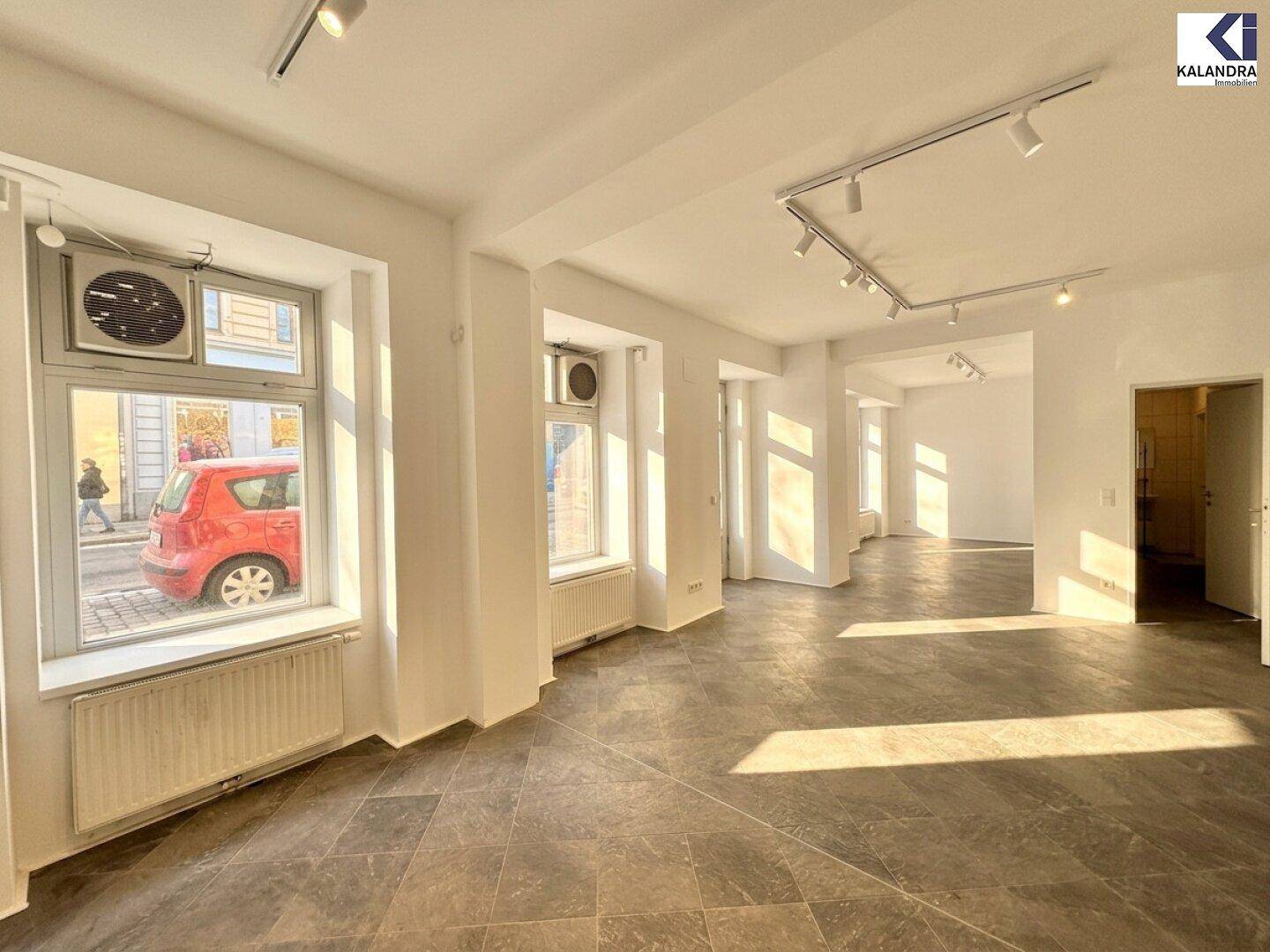 Heller Gewerberaum mit großen Fenstern, die einen Blick auf die Straße und vorbeifahrende Autos bieten.