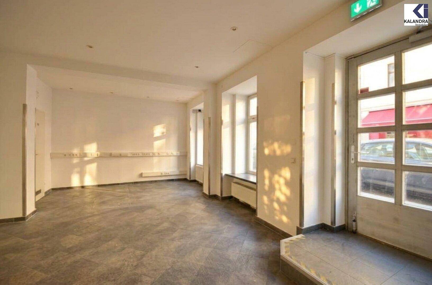 Heller Gewerberaum mit Eingangstür, Fliesenboden und Notausgangsbeschilderung an der Decke.