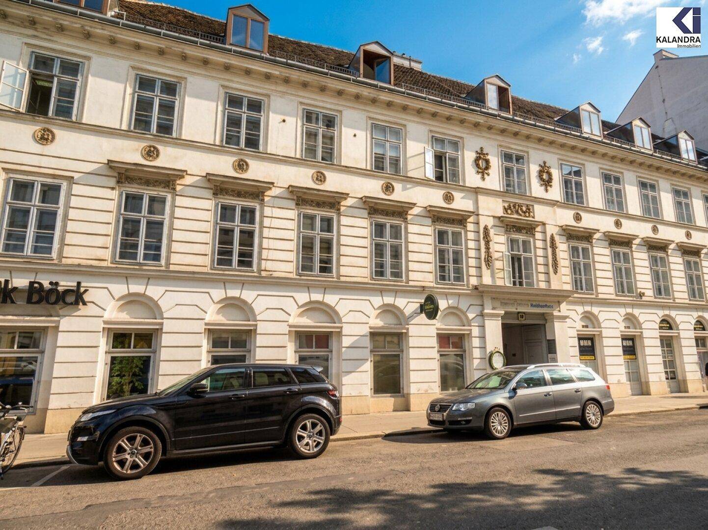 Breite Ansicht der historischen Gebäudefassade mit vielen Fenstern, Dachgauben und geparkten Fahrzeugen.