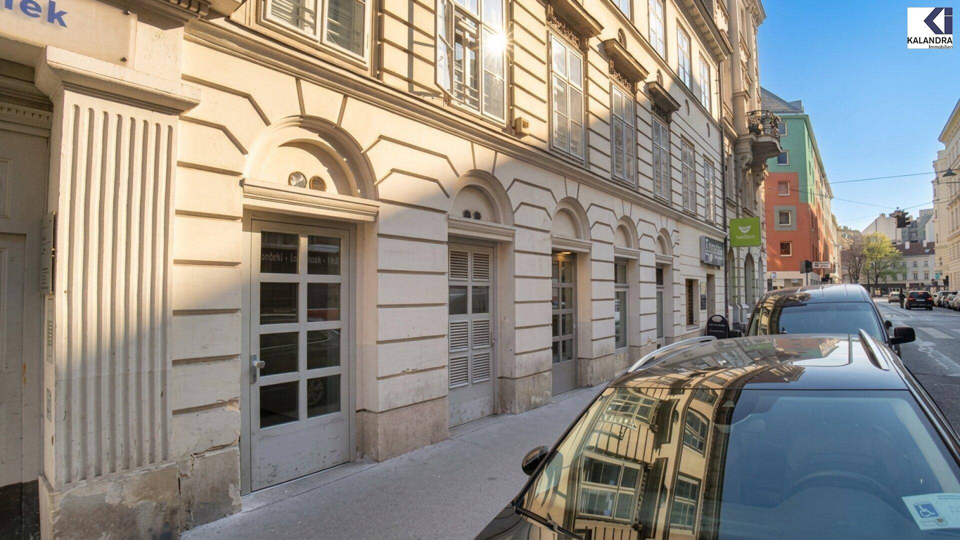 Historische Gebäudeansicht an einer belebten Straße mit geparkten Autos und mehreren Eingängen.