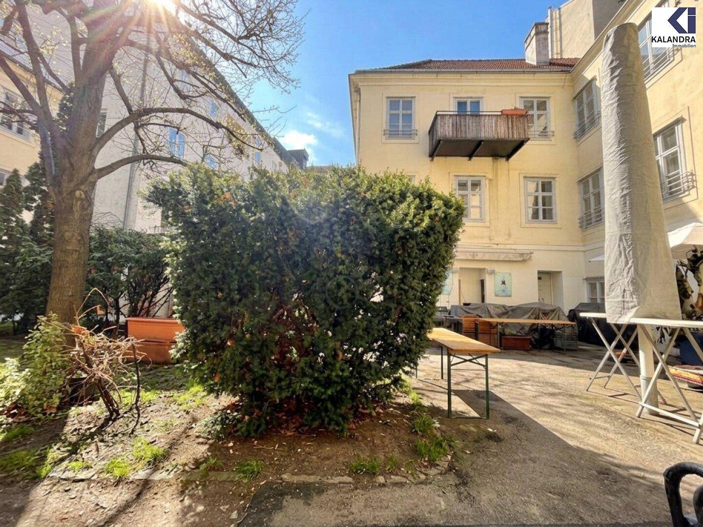 Grüner Innenhof mit Bäumen, Sträuchern und einem Gebäude im Hintergrund, ideal für Entspannung.
