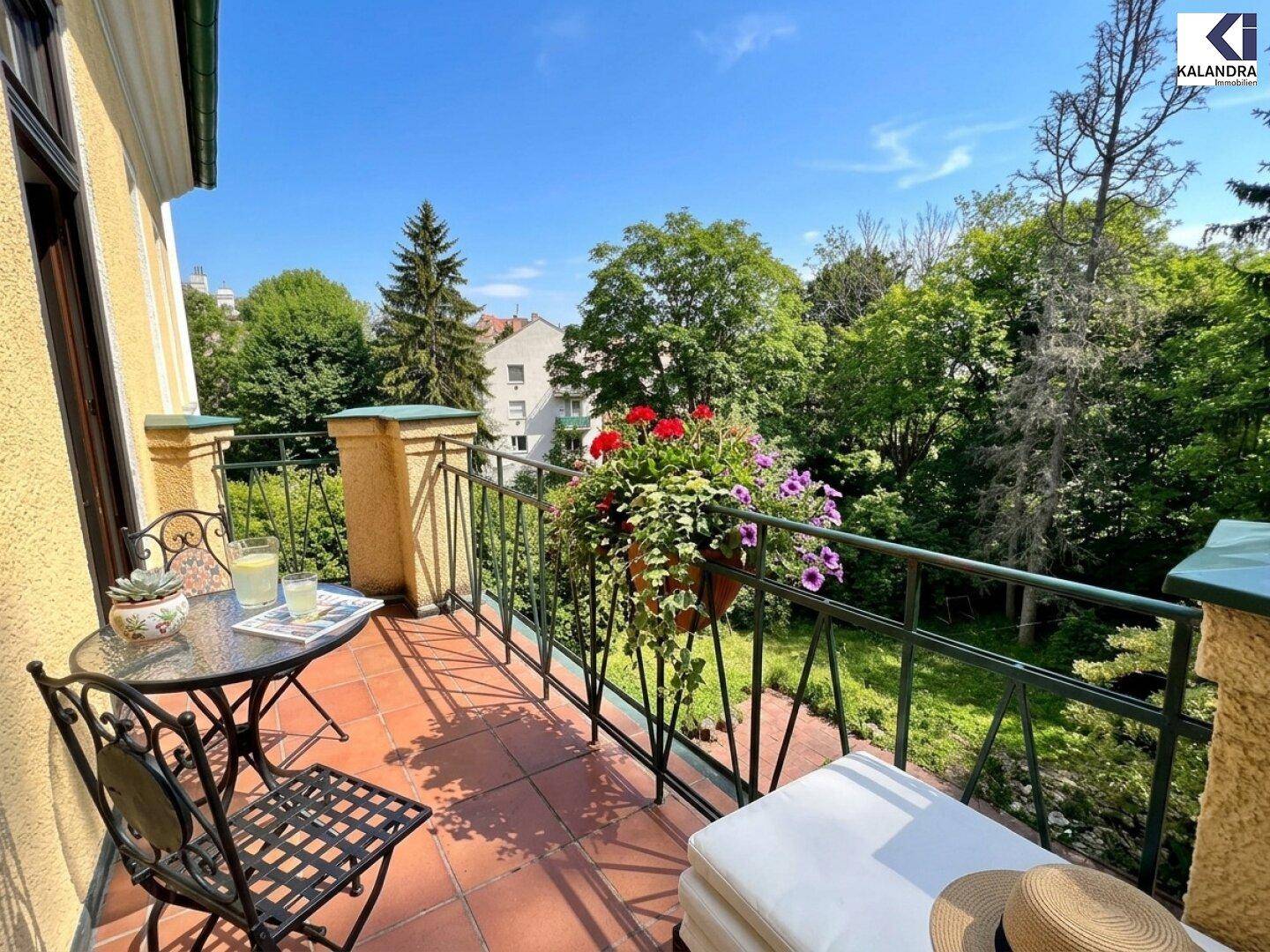 Sonniger Balkon mit Blumenkästen und einem kleinen Tisch, umgeben von einer grünen Landschaft.