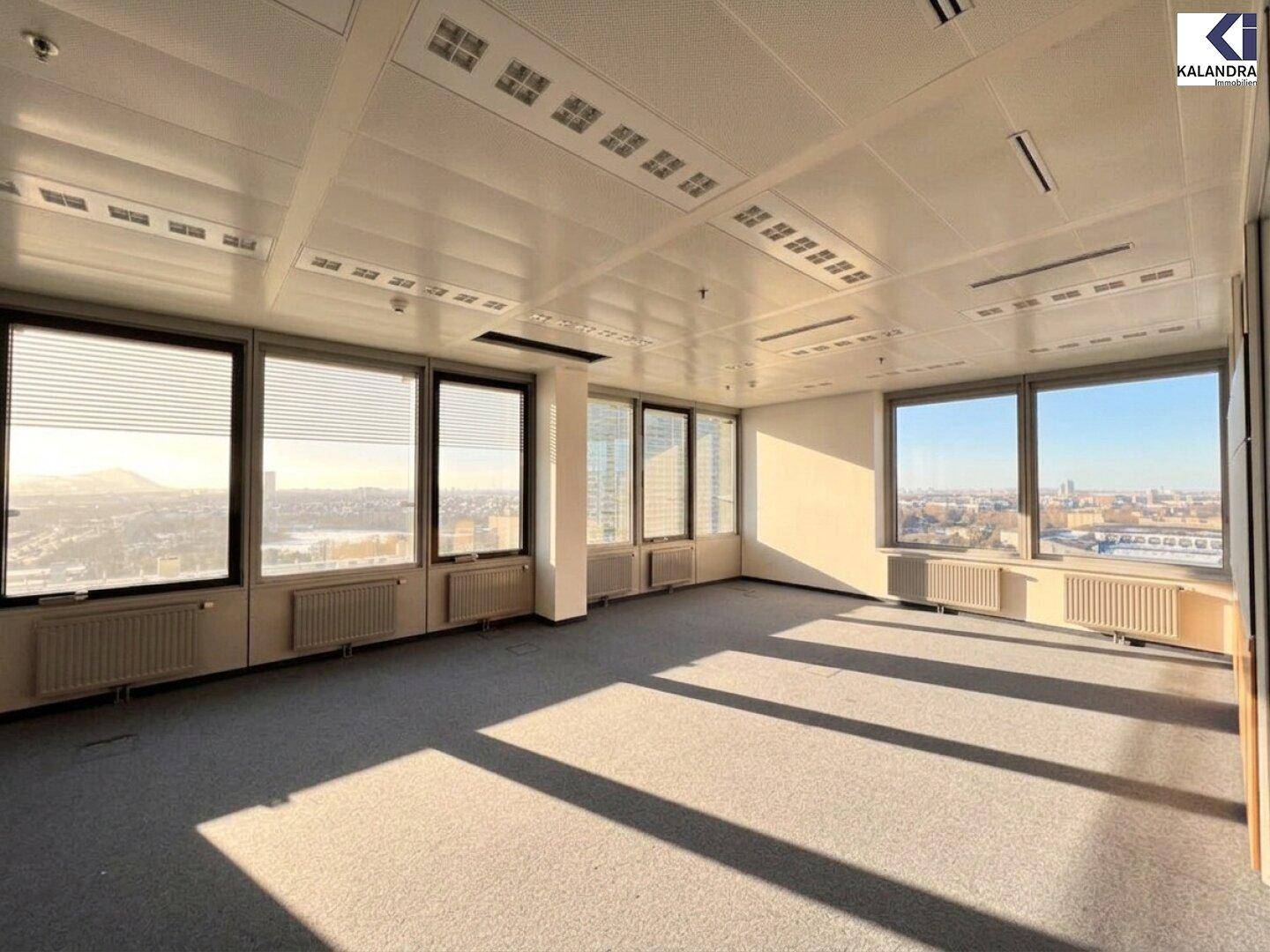 Helles Büro mit Teppichboden und breiten Fenstern, die einen Panoramablick auf die Stadt ermöglichen.