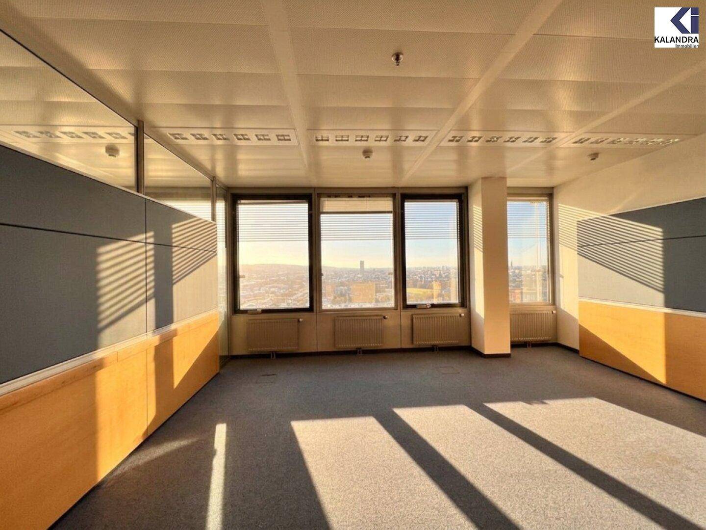 Bürofläche mit Teppichboden und Fenstern, die durch Jalousien vor direkter Sonneneinstrahlung geschützt sind.