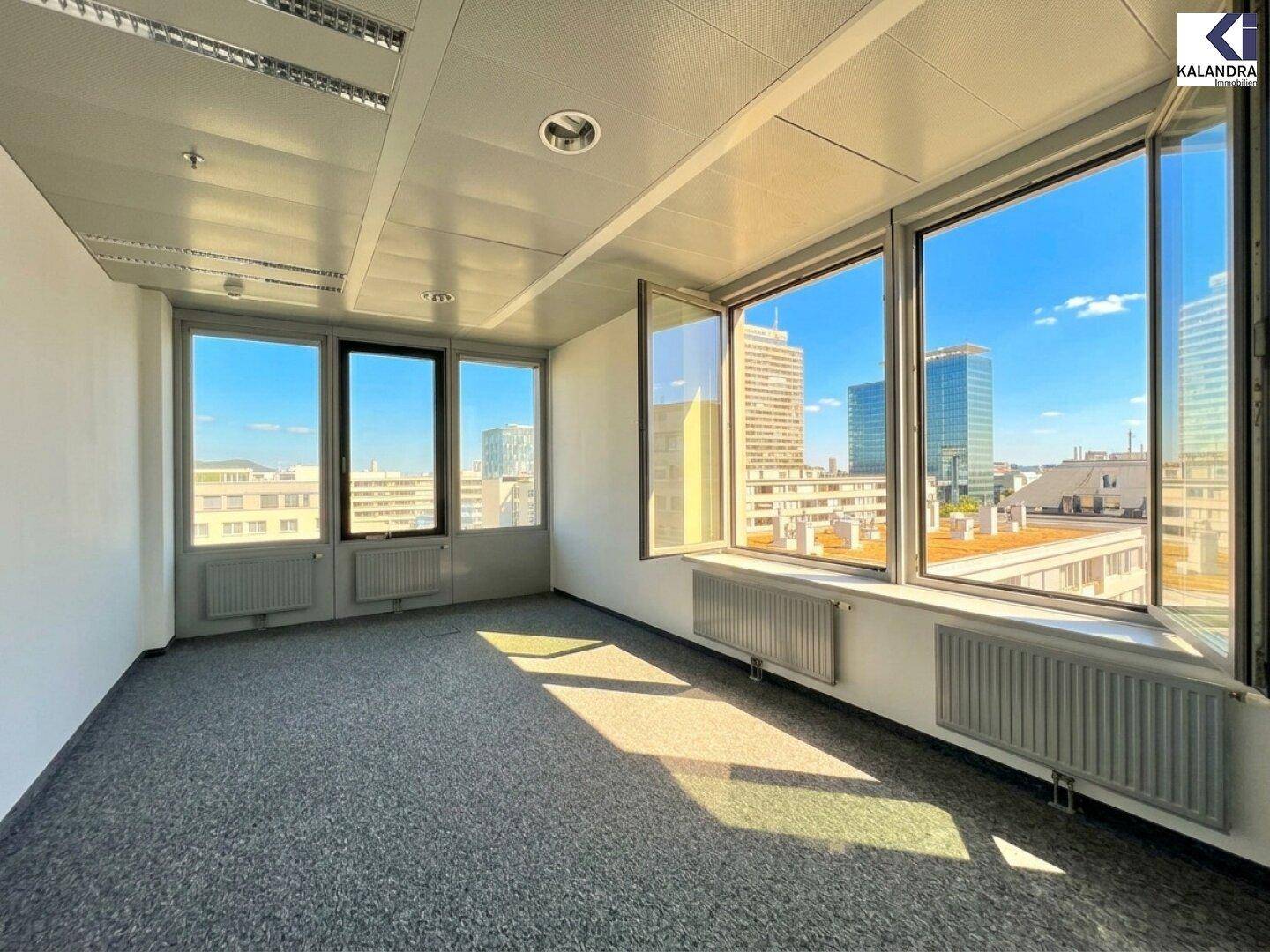 Büro mit Teppichboden und geöffneten Fenstern, die frische Luft und einen weiten Blick auf die Stadt ermöglichen.