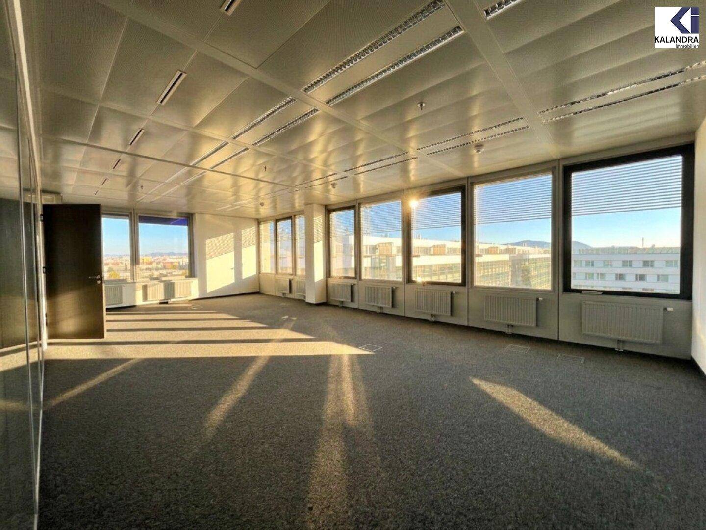 Heller Büroraum mit Teppichboden und großen Fenstern, die viel Tageslicht hereinlassen und eine weite Aussicht bieten.