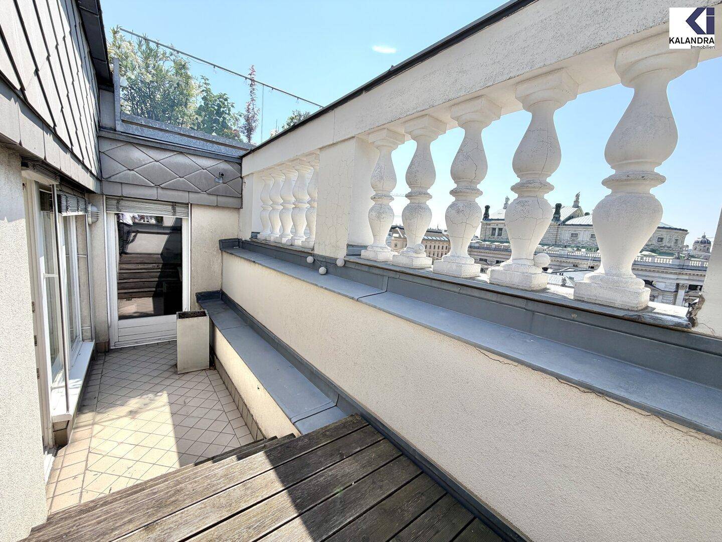 Geräumige Dachterrasse mit klassischer Balustrade, Holzboden und Blick auf die umliegenden Gebäude.