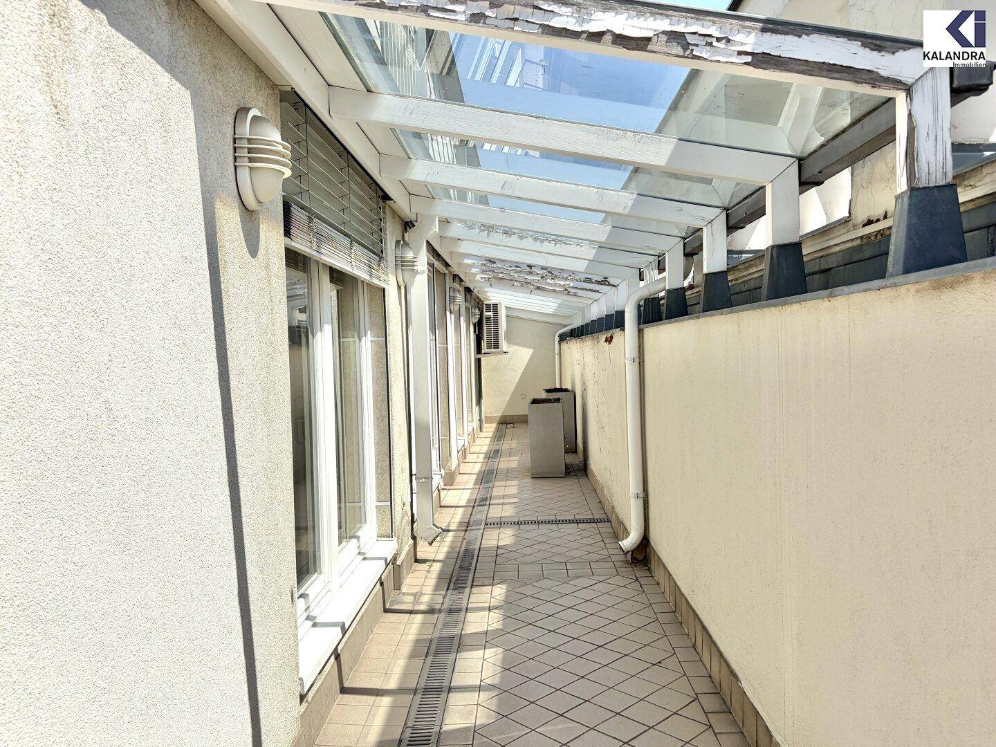 Überdachter Außenbereich mit Fliesenboden und Glasdach, der Schutz vor Witterung bietet.