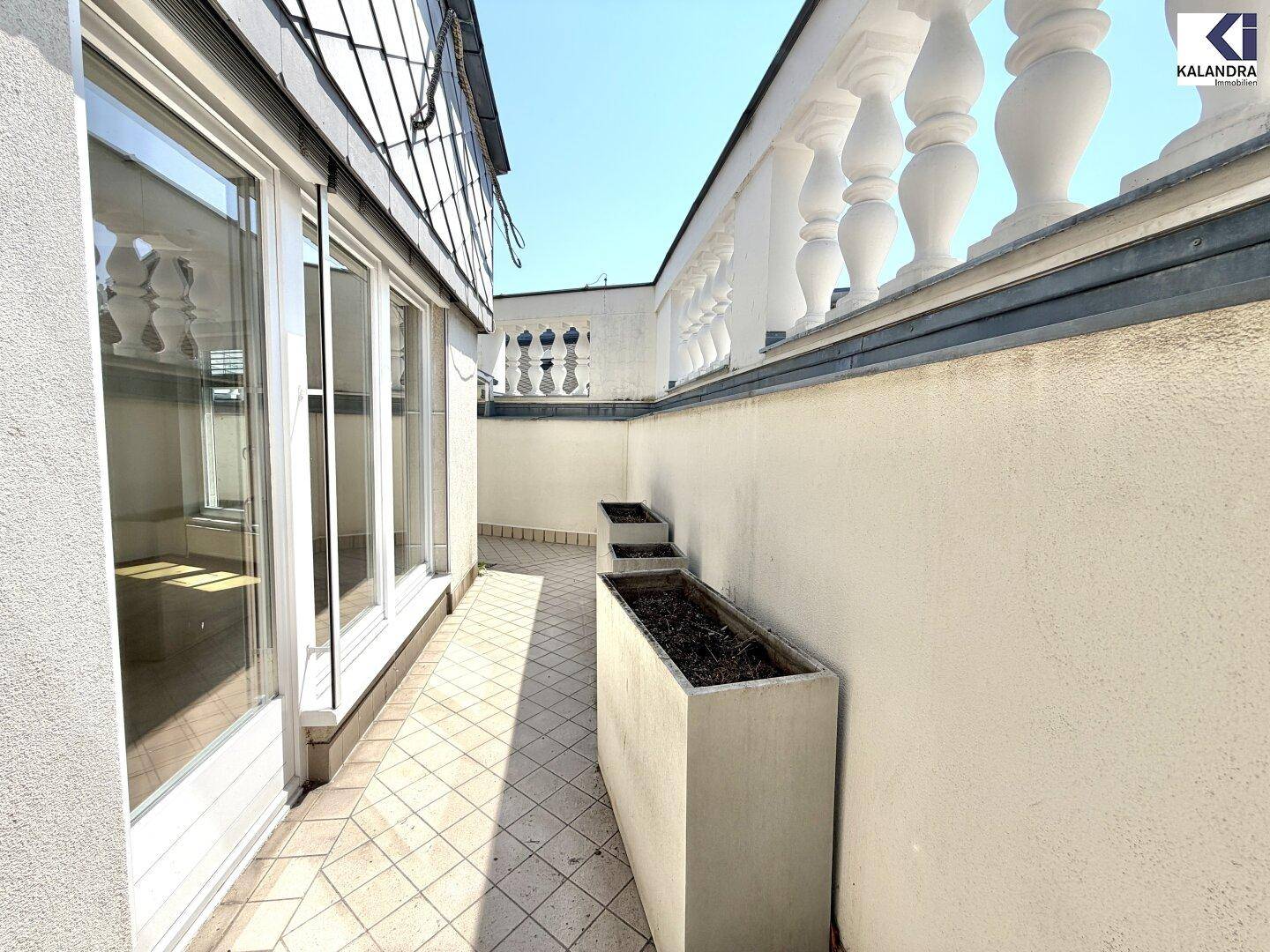 Langer Balkon mit Fliesenboden und Pflanzkübeln, der direkten Zugang zum Innenbereich ermöglicht.