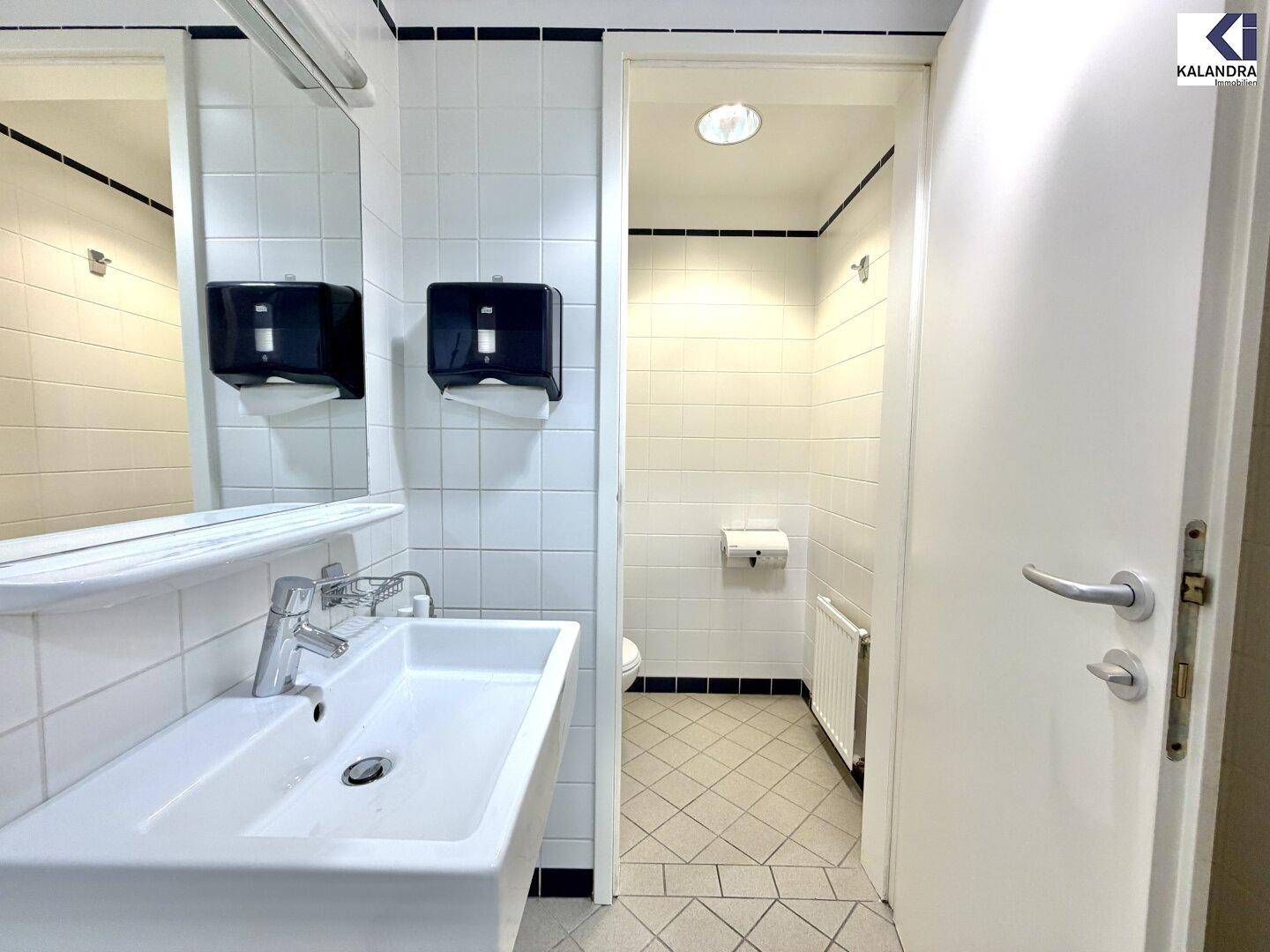 Funktionales Badezimmer mit weißen Fliesen, Waschbecken und separatem WC-Bereich.
