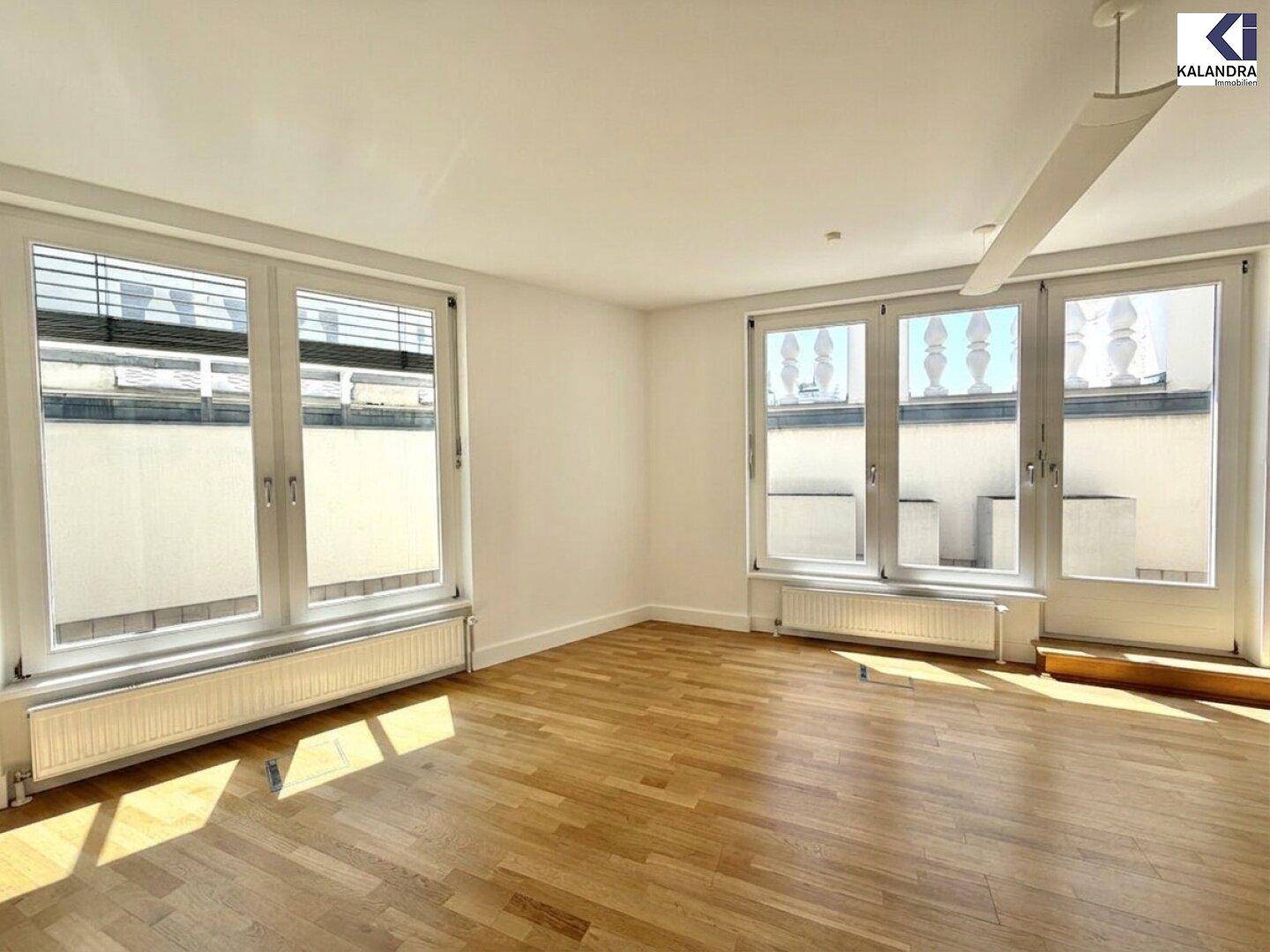 Lichtdurchfluteter Raum mit Holzboden und großen Fenstern, die einen hellen und einladenden Eindruck vermitteln.
