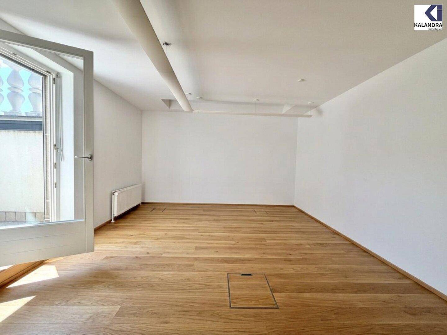 Geräumiger, leerer Raum mit Holzboden und einer offenen Tür, die viel frische Luft hereinlässt.