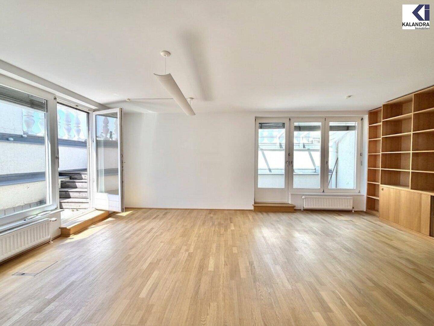 Heller Wohnraum mit Holzboden, großen Fenstern und einem integrierten Holzregal.