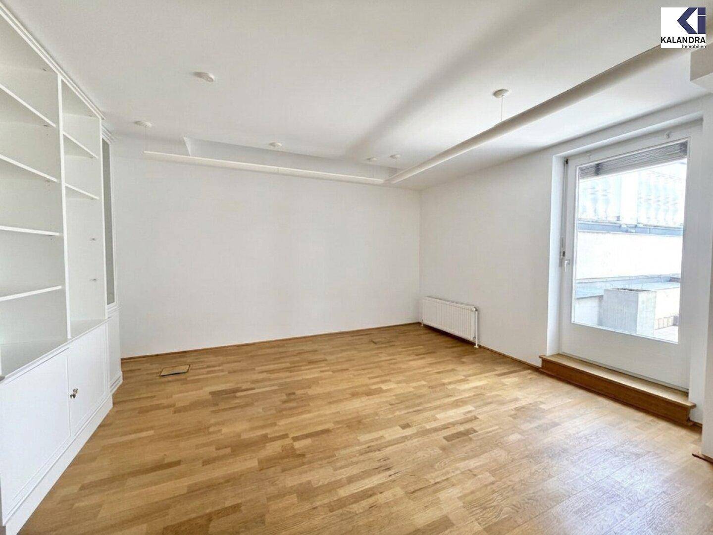 Geräumiger Raum mit Holzboden, weißem Einbauregal und einem Fenster, das Tageslicht spendet.