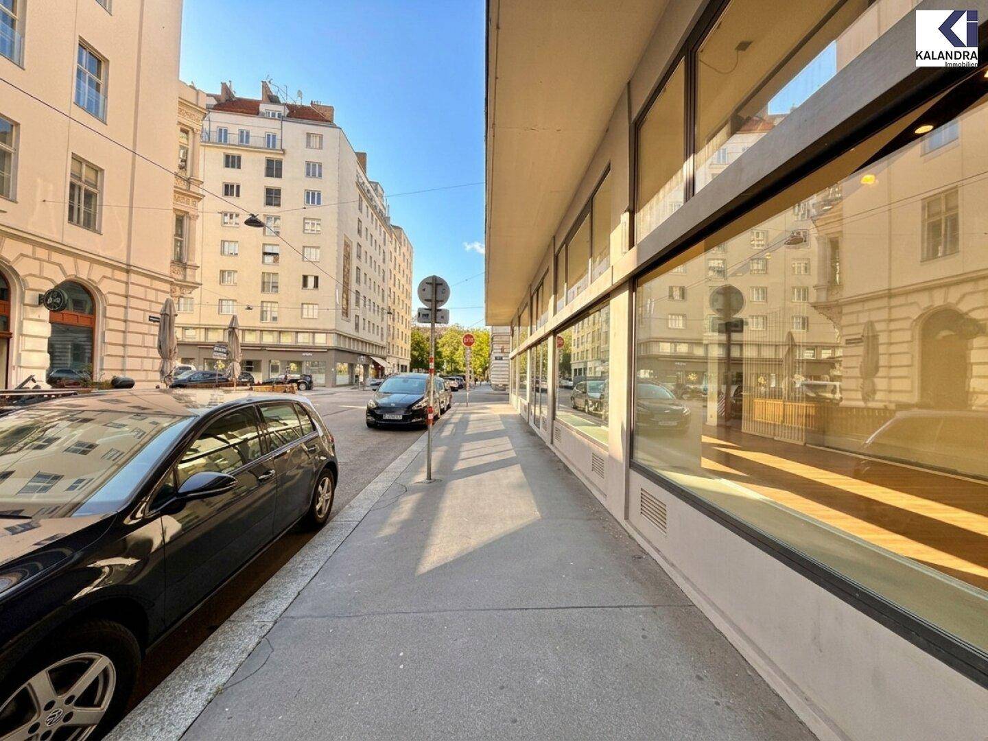 Lange Geschäftsfassade mit durchgehender Fensterfront entlang eines belebten Bürgersteigs in der Stadt.