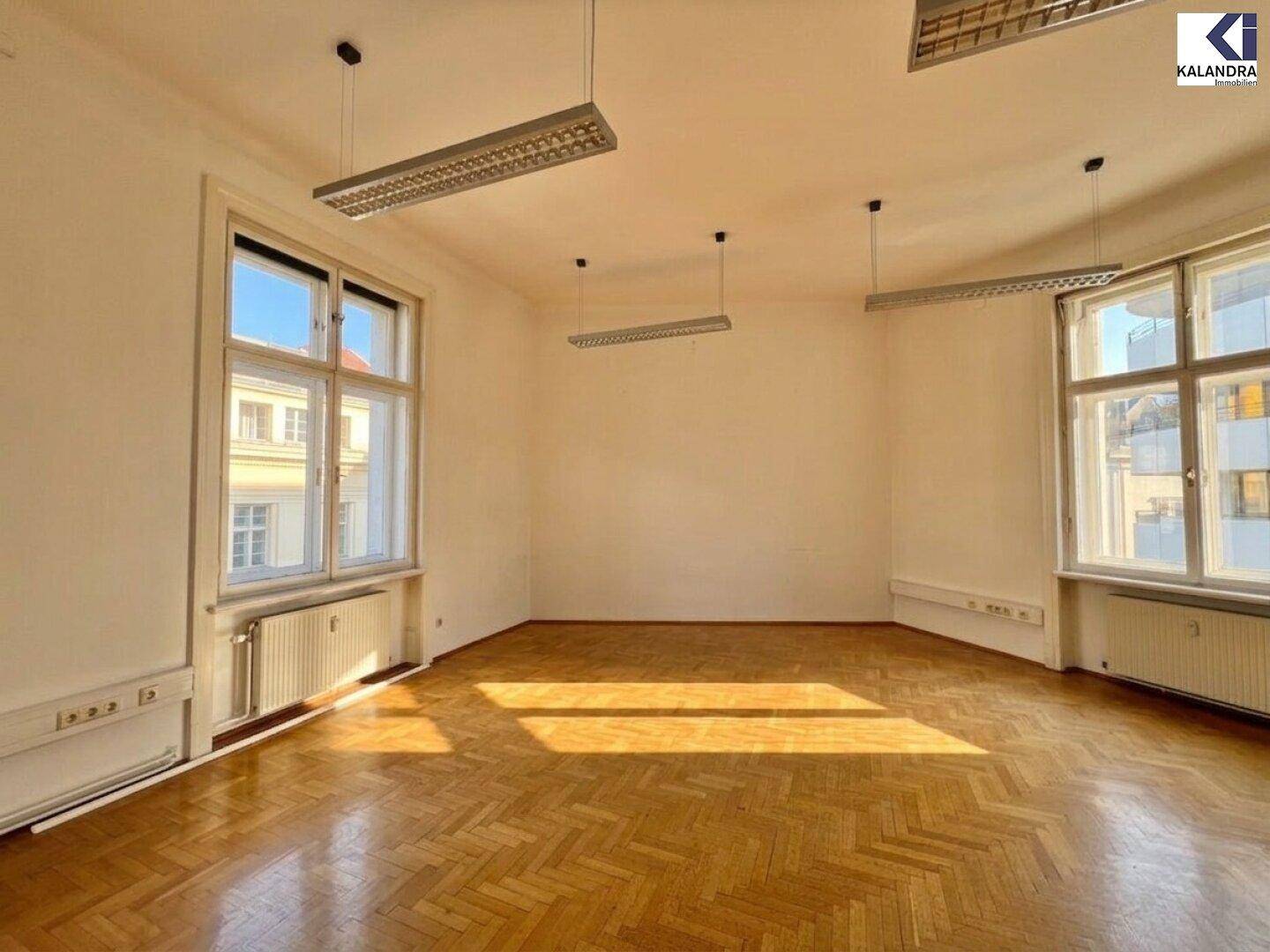 Heller Büroraum mit Fischgrätparkett und großen Fenstern, die viel Tageslicht bieten.
