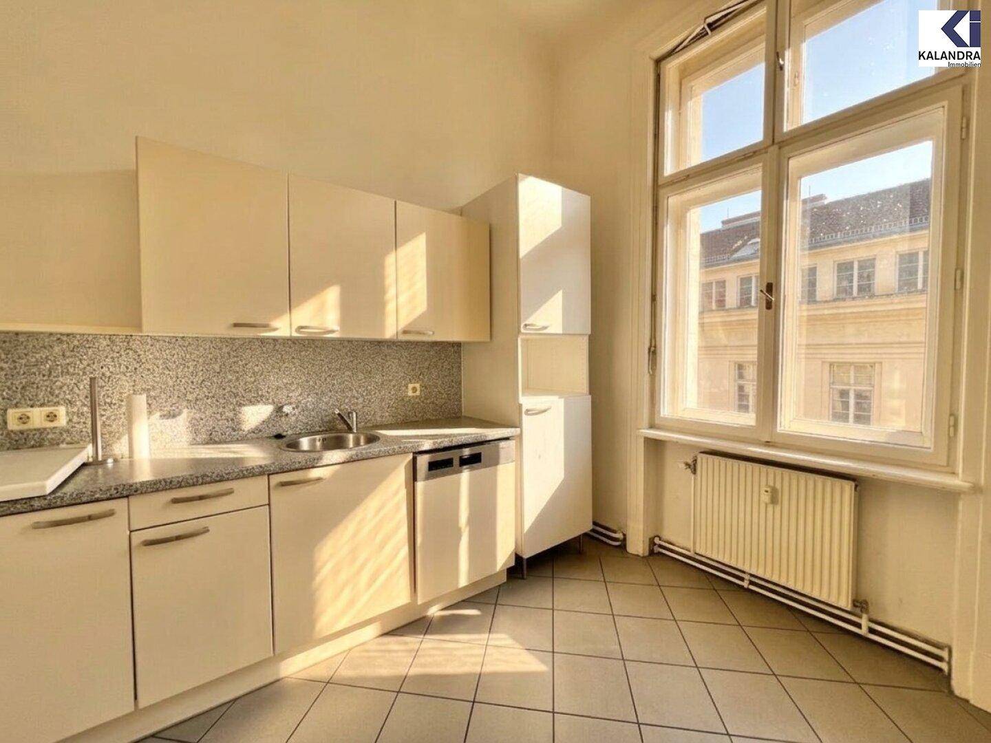 Funktionale Küche mit hellen Schränken, Fliesenboden und großem Fenster.