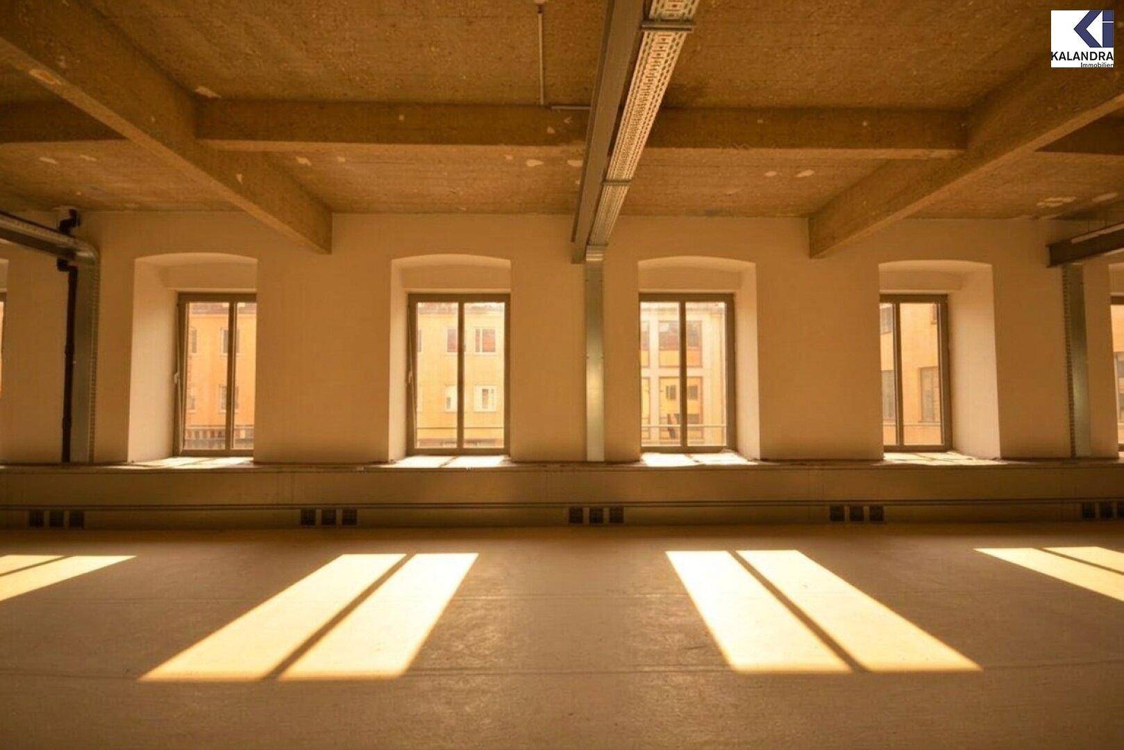 Reihe von Fenstern in einem hellen Büroraum, die viel Tageslicht hereinlassen und eine städtische Aussicht bieten.