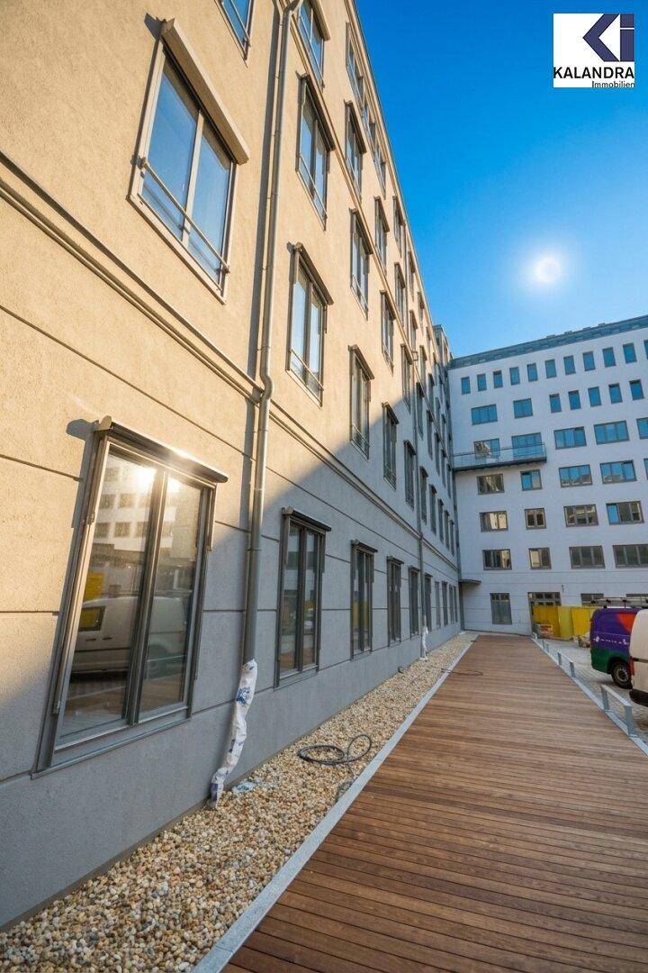 Seitenansicht eines modernen Gebäudes mit Holzsteg und Kiesbeet unter strahlendem Sonnenschein.