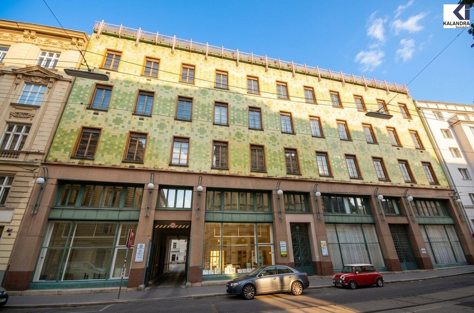 Historische Gebäudefassade mit kunstvollen Details und großen Fenstern an einer belebten Straße.