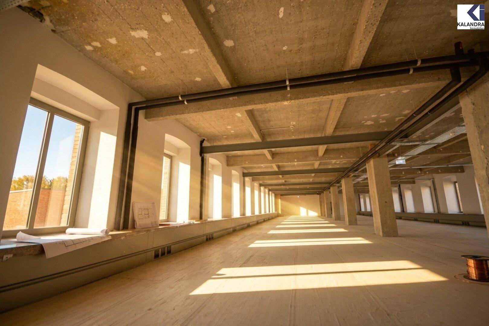 Langer, heller Büroraum mit vielen Fenstern und sichtbaren Betonstrukturen, bereit für den Ausbau.