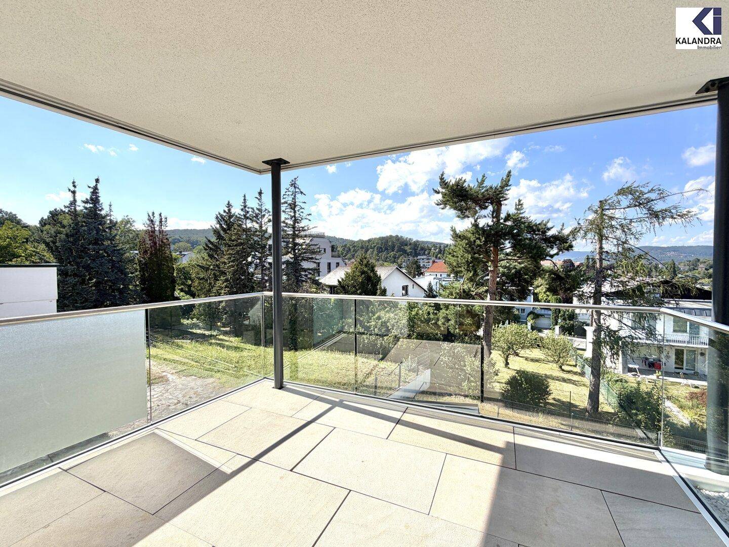 Heller Balkon mit moderner Glasbrüstung und sonnigem Ausblick auf die umliegende Landschaft.