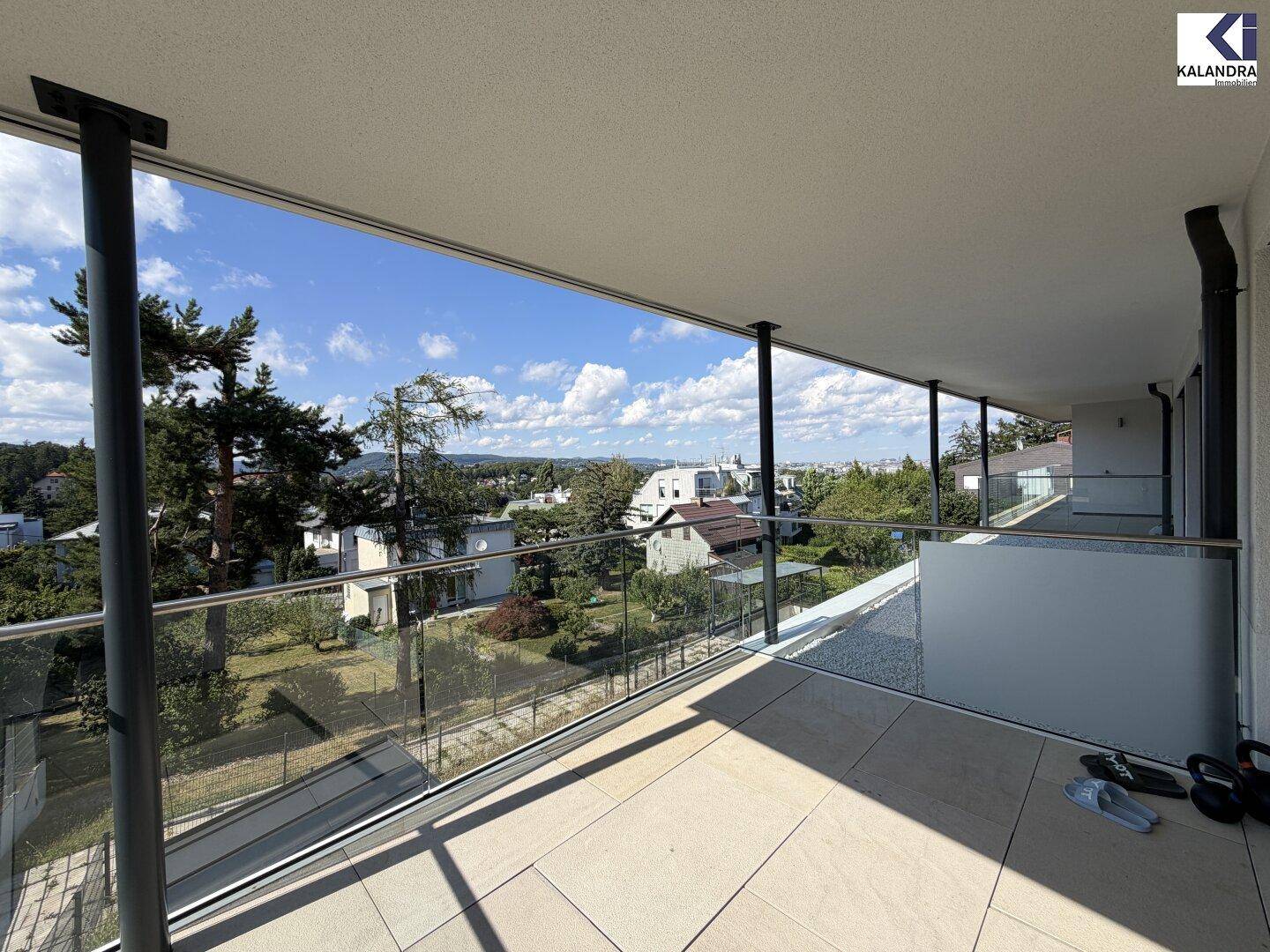 Langer Balkon mit Fliesenboden und weitem Blick über die Dächer und grüne Umgebung.