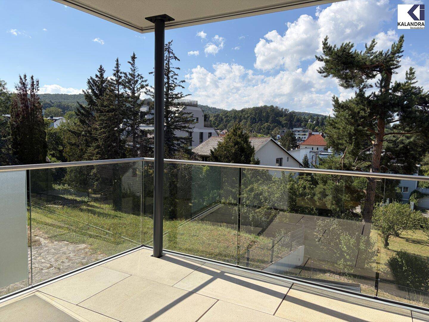 Sonniger Balkon mit moderner Architektur und unverbautem Blick auf die bewaldete Hügellandschaft.