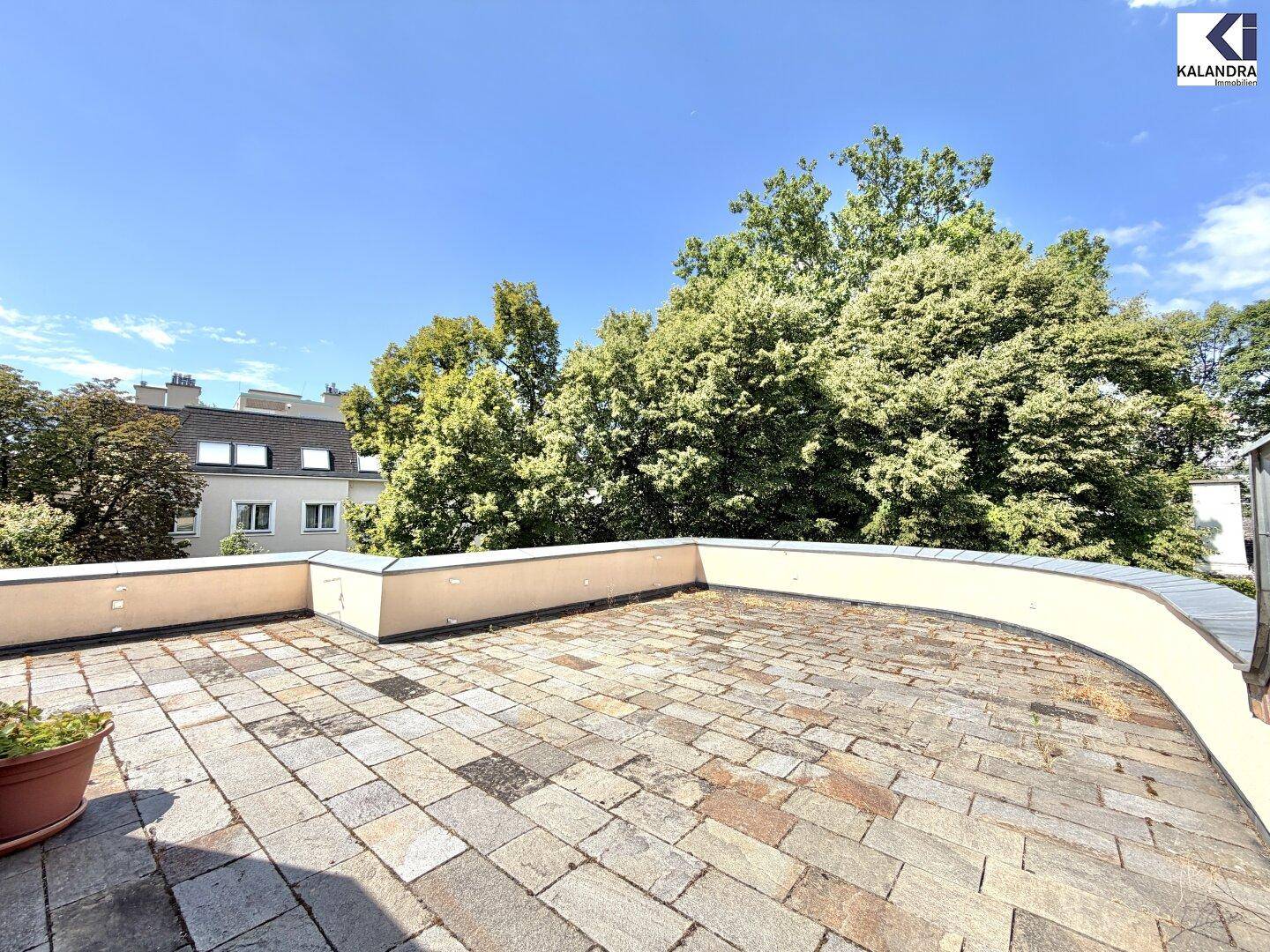 Weitläufige Dachterrasse mit Steinplatten und Blick auf umliegende Gebäude und Bäume.