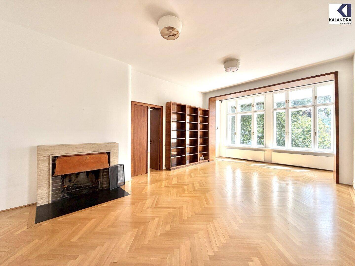 Helles Wohnzimmer mit klassischem Kamin, Fischgrätparkett und großen Fenstern.