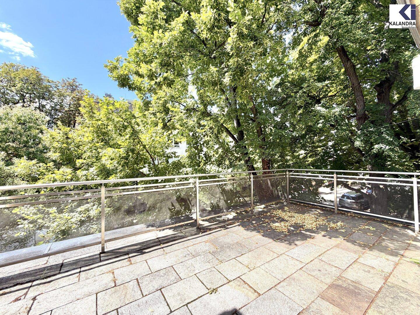 Geräumiger Balkon mit Glasgeländer und Blick auf üppiges Grün und Bäume.