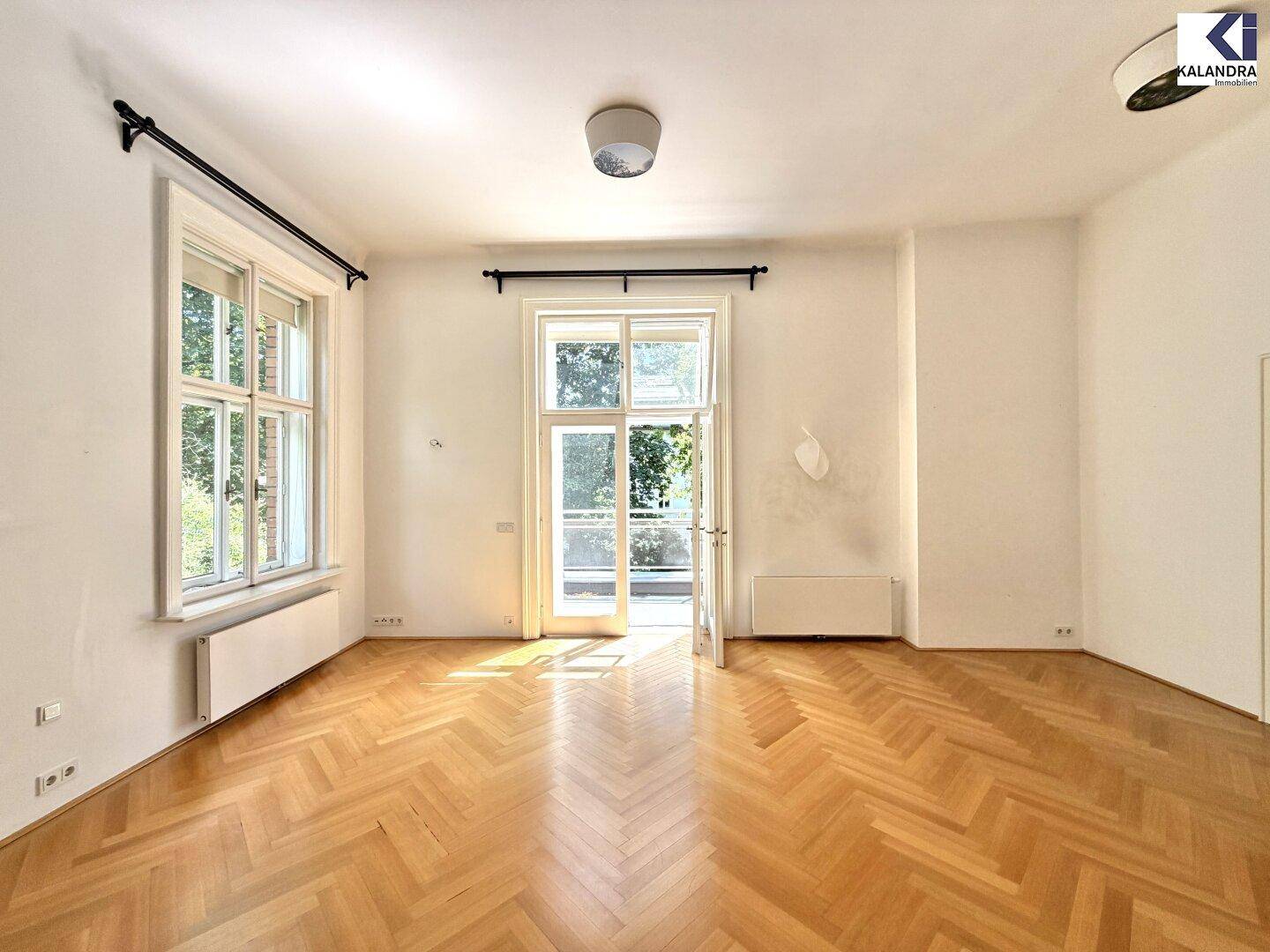 Helles Zimmer mit Fischgrätparkett und direktem Zugang zu einem Balkon.