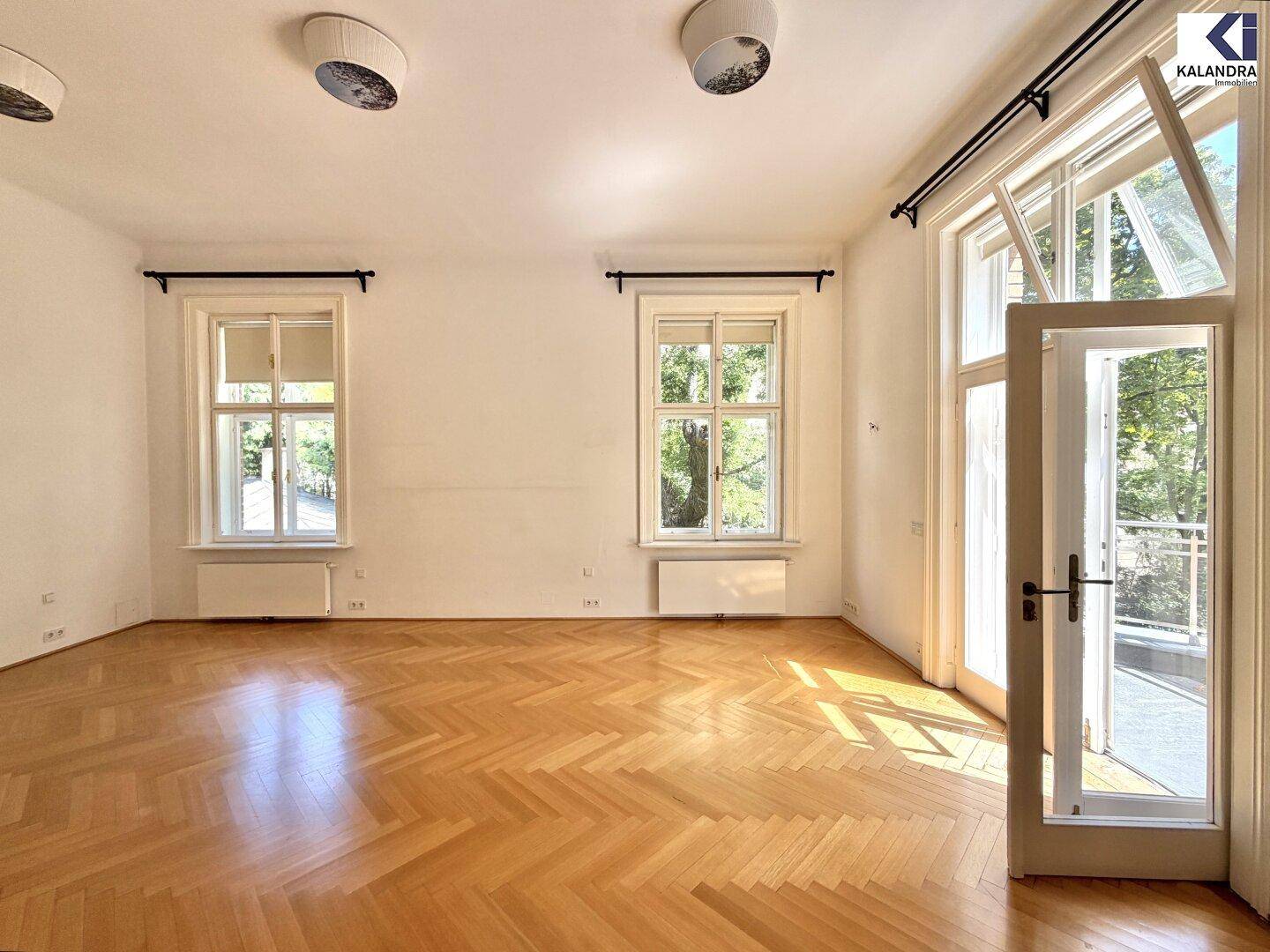 Großzügiges Zimmer mit Fischgrätparkett, hohen Fenstern und Balkonzugang.