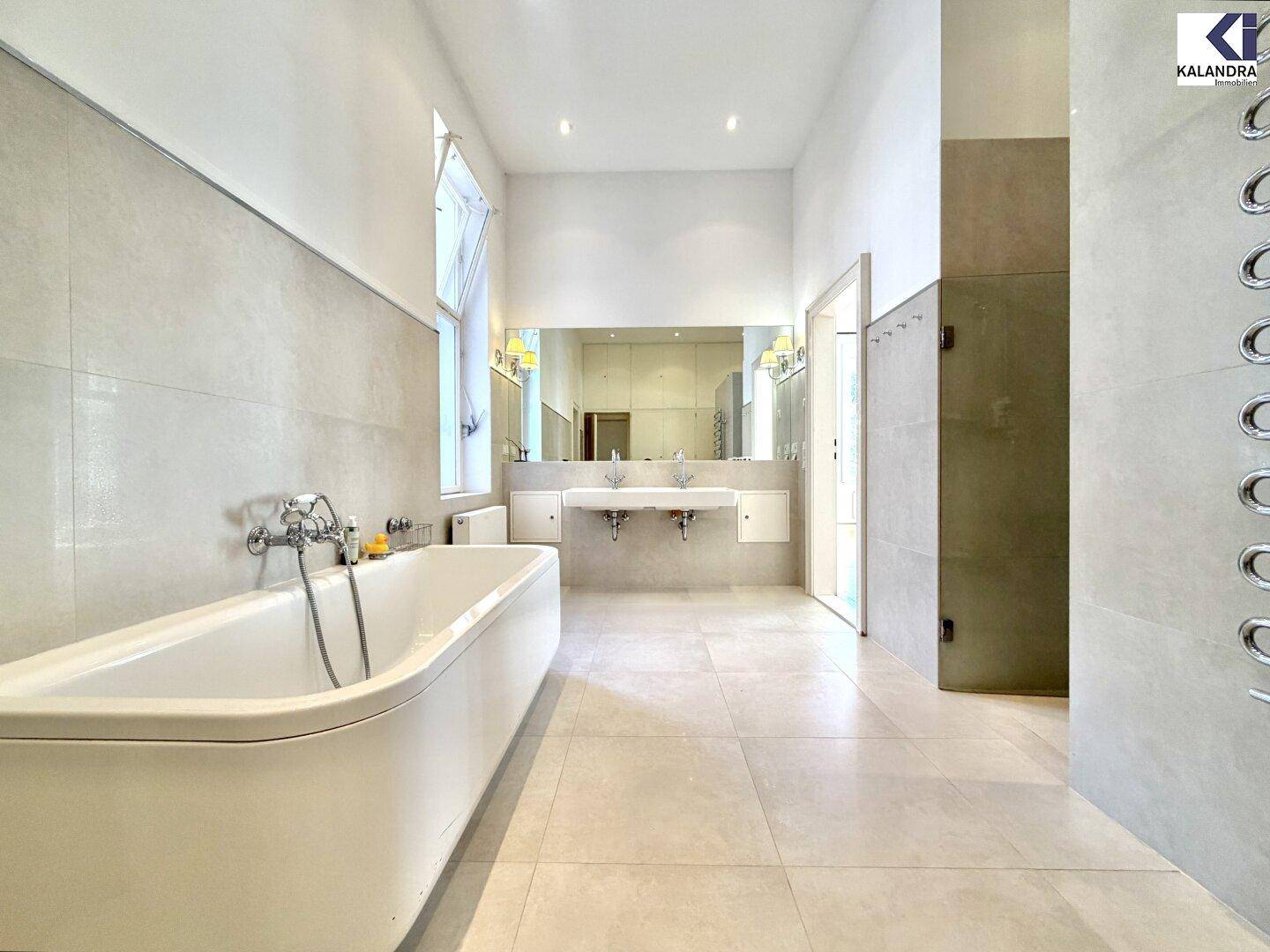 Modernes Badezimmer mit freistehender Badewanne, Doppelwaschbecken und großen Fliesen.