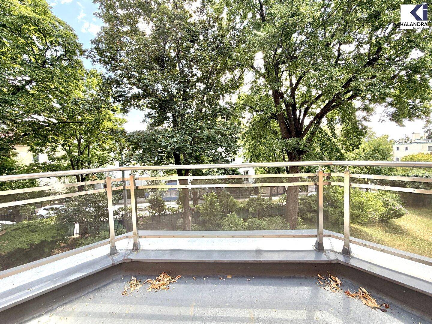 Kleiner Balkon mit Glasgeländer und Blick auf grüne Bäume und die Umgebung.