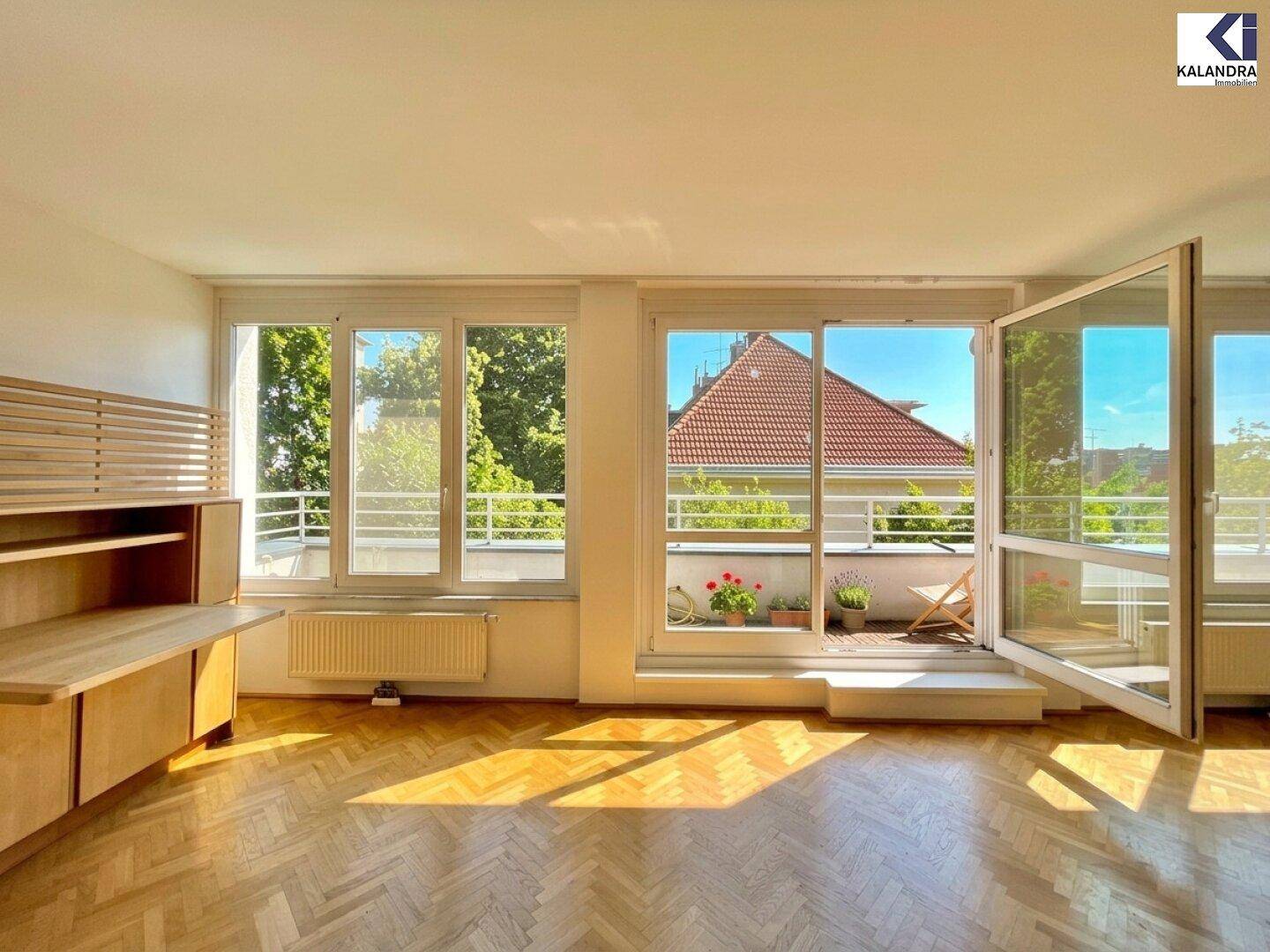 Helles Wohnzimmer mit Fischgrätparkett und Zugang zu einem sonnigen Balkon mit Blick ins Grüne.