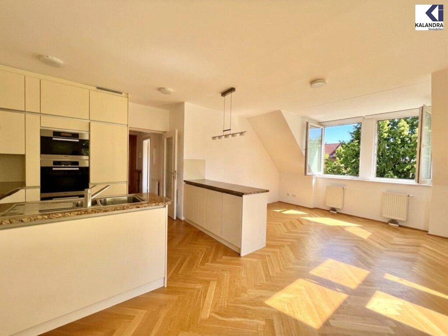 Offener Wohnbereich mit moderner Einbauküche, Fischgrätparkett und viel Tageslicht.