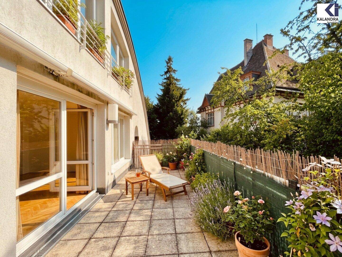 Sonnige Terrasse mit Liegestuhl, Blumen und Blick auf ein charmantes Nachbarhaus.