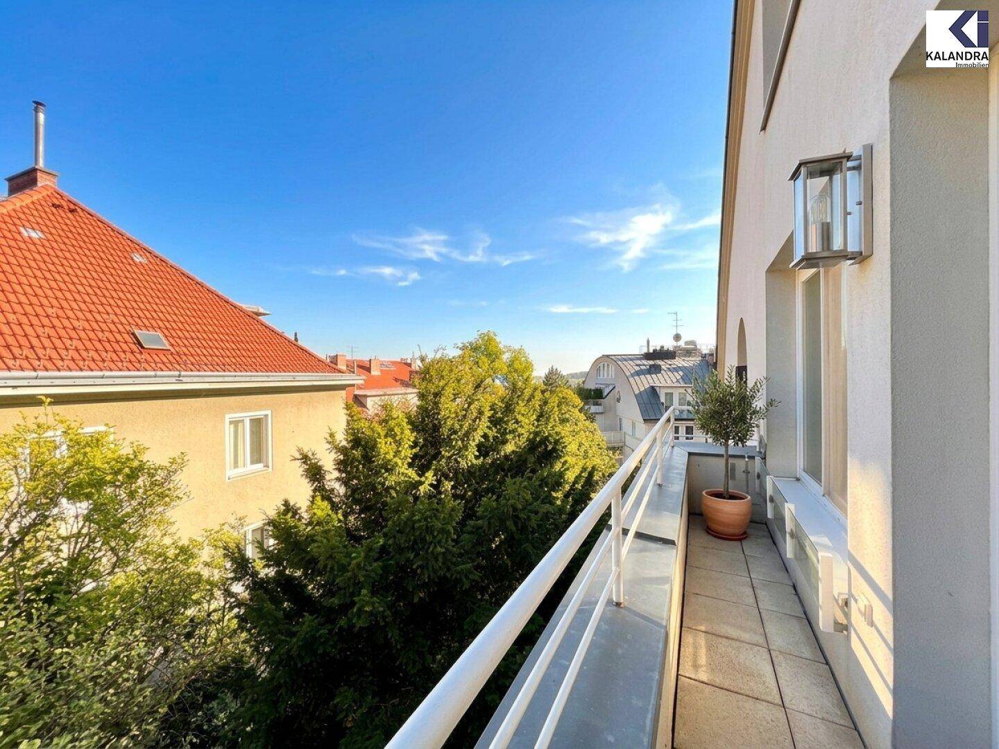 Schmaler Balkon mit Geländer und Ausblick auf die umliegenden Dächer und grüne Bäume.