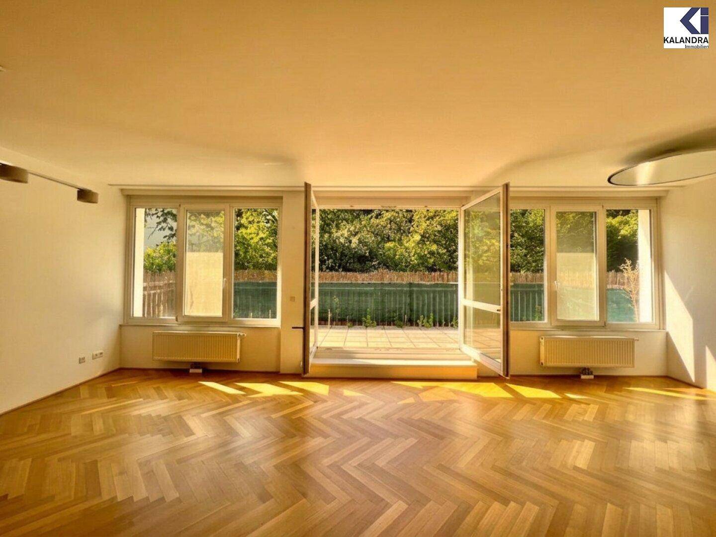 Großzügiges Wohnzimmer mit Fischgrätparkett, großen Fenstern und Zugang zur Terrasse.