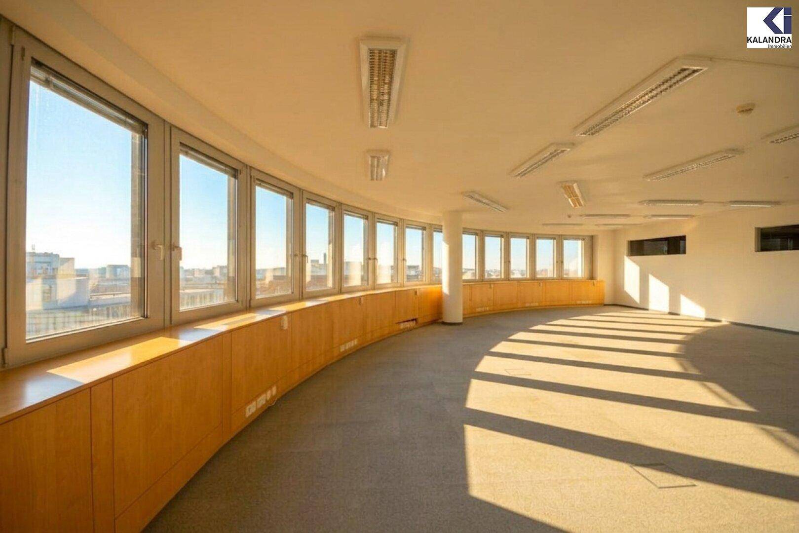 Großer, leerer Raum mit vielen Fenstern, die einen weiten Blick über die Stadt bieten und viel Tageslicht hereinlassen.